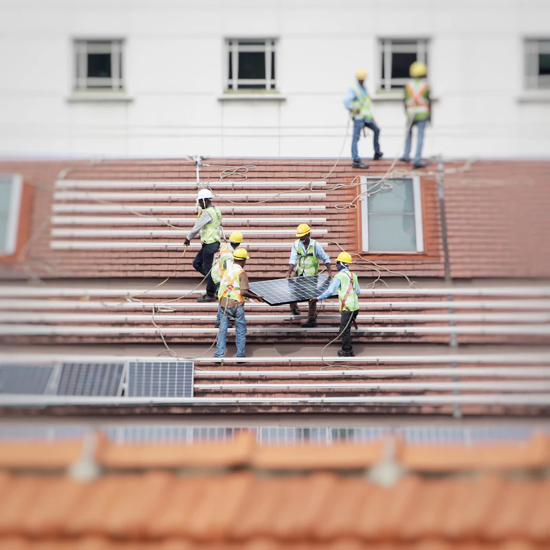 Team installateurs met helmen draagt panelen over een pannendak