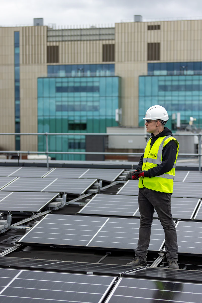 Installateur met helm en hesje tussen zonnepanelen op een plat dak
